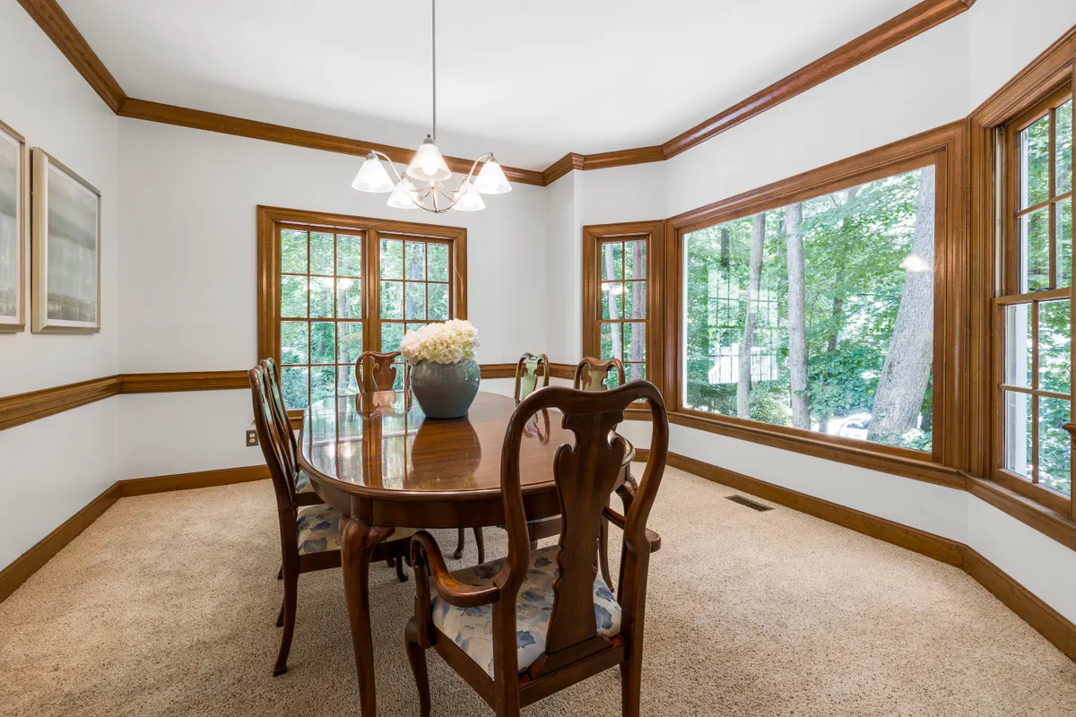 A staged dining room with an oval wooden table, six chairs, a chandelier and bay windows